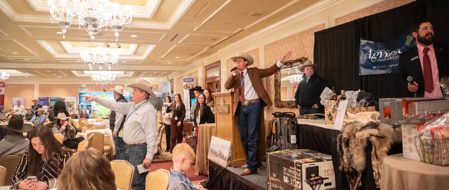 Tanner Beymer leading a live auction on stage in a grand gala room